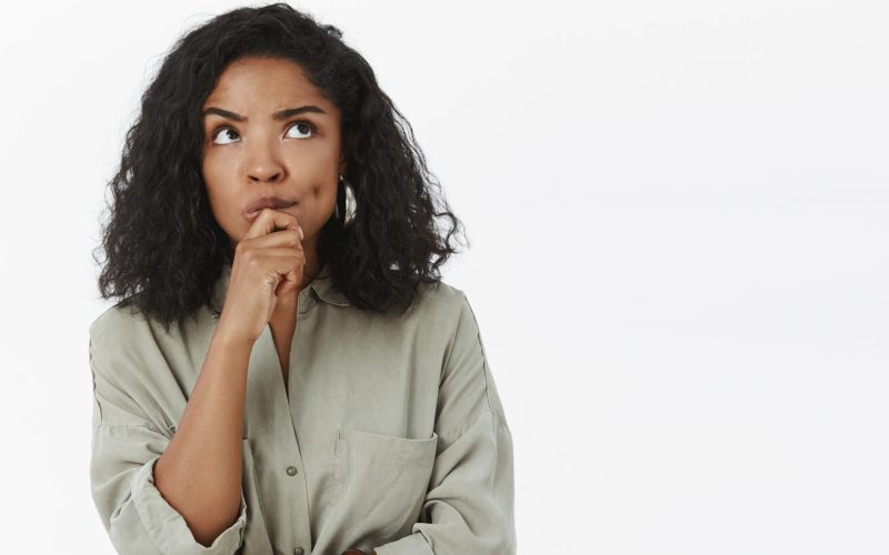Girl needs make up excuse thinking standing focused in thoughtful pose holding hand on chin frowning looking up posing over gray background determined and concentrated on thought. Copy space